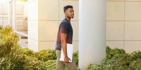 African American man walks into a building carrying a laptop in an article about planning for the cost of college.